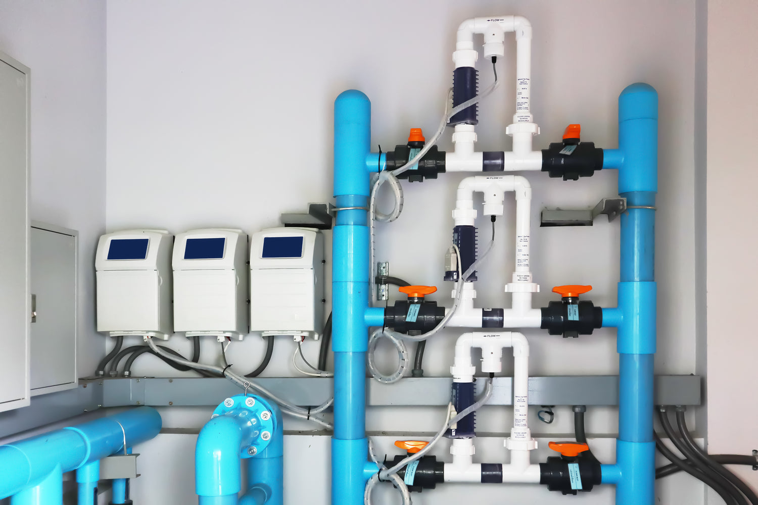 Auf dem Bild ist Pool-Wassertechnik zu sehen. Es sind mehrere Pumpen mit hellblauen Rohren aus Kunststoff verbunden. Alles ist verkabelt und bereit zur Inbetriebnahme